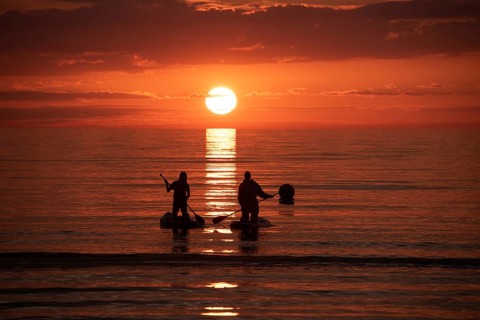 Two people paddling in the calm sea at sunset on stand-up paddle, silhouettes against a bright