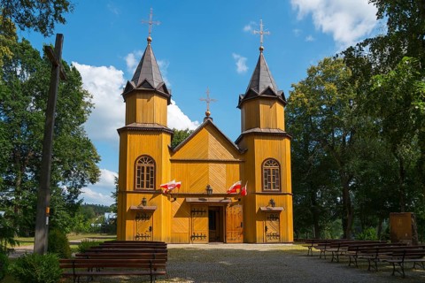 Wooden church with two towers, surrounded by trees and under a blue sky in the sunshine, wooden
