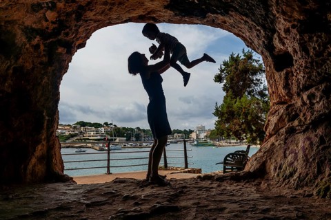 Silhouette of a mother lifting her son inside a cave with a view of the harbor in puerto cristo,