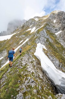 Two mountaineers with helmets on a narrow hiking trail, ascent to the Ackerlspitze, clouds moving