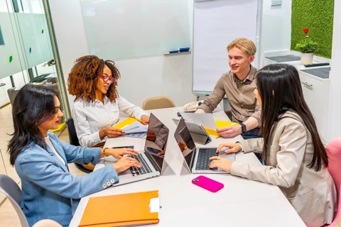 Four businesspeople using laptops and collaborating on a project in a modern coworking space,