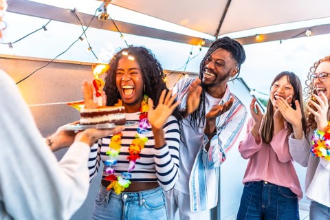 African woman celebrating her birthday with her multiracial friends during sunset in a terrace