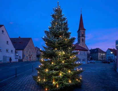 Illuminated Christmas tree on the village square at dusk, St Bartholomew's Church in the