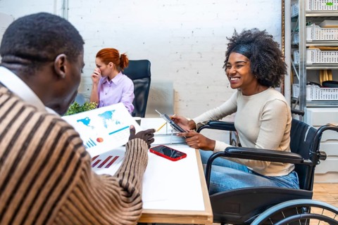 Cheerful and smiling african woman with disability sitting on wheelchair and colleague discussing