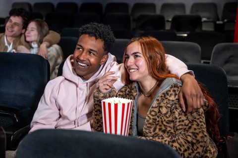 Happy couple sharing popcorn while watching a movie at the cinema, enjoying a night out with