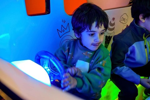 Young boy playing with toy car steering wheel, enjoying entertainment in colorful amusement park