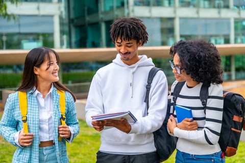 Happy multi-ethnic university students reading notes together standing outside the university in a