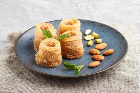 Kunafa, traditional arabic sweets in blue ceramic plate on a gray concrete background. side view,