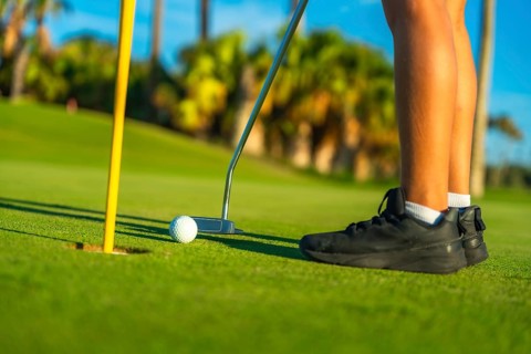 Person putting golf ball in a green course, low section