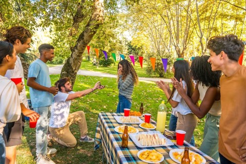 Caucasian young man kneeling to propose marriage to woman during picnic with multi-ethnic friends