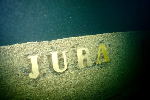 The lettering 'Jura' can be seen on a weathered shipwreck covered with mussels, quagga triangle