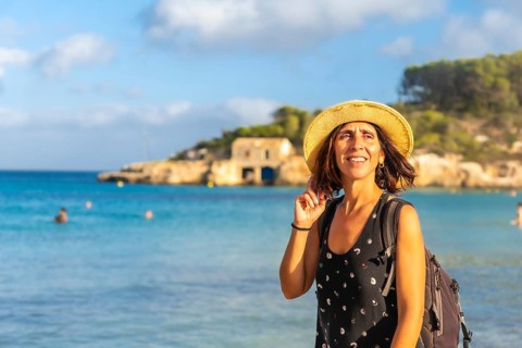 Female tourist with backpack and straw hat enjoying summer holidays on beautiful s'amarador beach