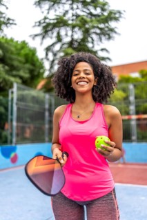 Vertical portrait of a latin female pickelball player standing smiling at camera in an outdoor