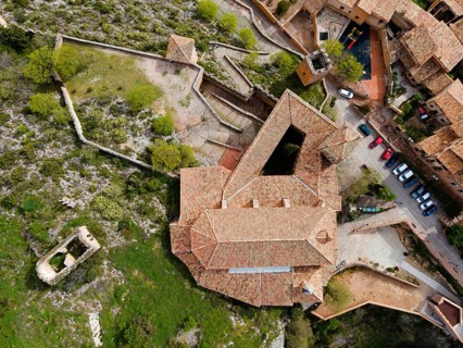 An aerial view of a historic fortress with tiled roofs and surrounding buildings on stony terrain,