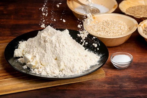 Flour is sprinkled over curd cheese, surrounded by baking ingredients on a wooden table