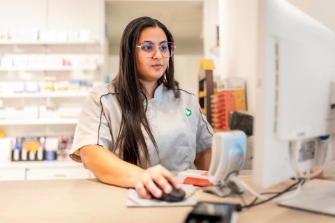 Young female pharmacist looking for a product in the inventory using computer