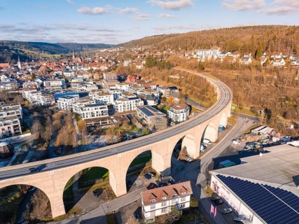 Aerial view of a town with viaduct, surrounded by hills and forests, under a blue sky, Nagold,