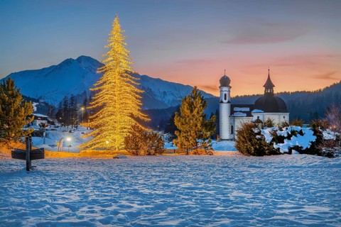 Seekirchl with artificially illuminated winter fir tree and Hocheder 2797m at dusk in winter,