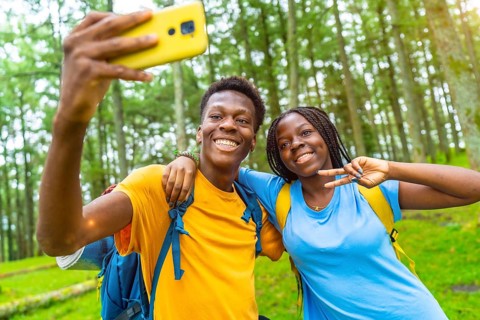 Cheerful african friends taking selfie gesturing victory with hand while hiking in the forest