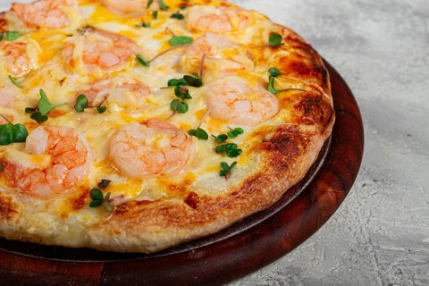 Four cheese pizza with shrimp and fresh microgreens, served on a wooden board, homemade, no people