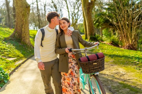 Young couple walking through park with bicycle, enjoying romantic moment together on sunny day