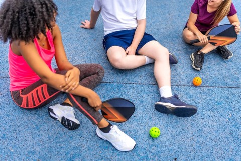 Latin woman and friends talking sitting on a pickelball court after playing together