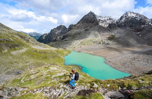 Hiker with rucksack looking at a turquoise-coloured mountain lake under a cloudy sky, Gradensee,