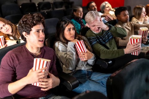 Young people and adults experiencing fear and suspense while watching a horror movie at the cinema,