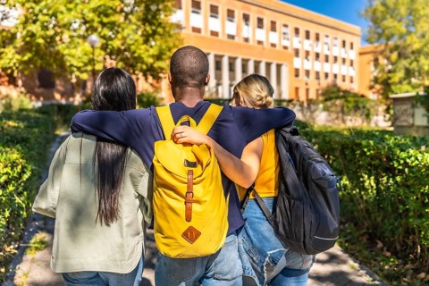 Rear view of three multi-ethnic students embracing while walking together to the university