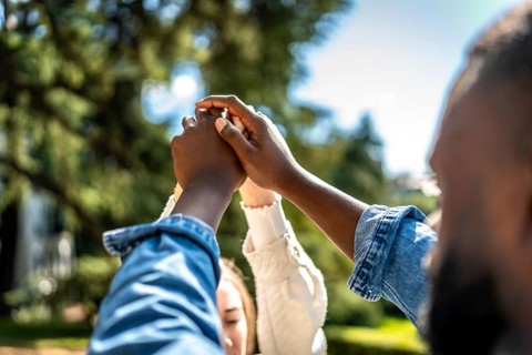 Multi-ethnic couple holding hands and raising them in a park