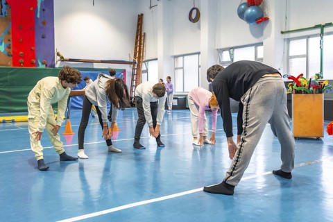 Teenagers bending forward and touching toes while exercising together in school gym class