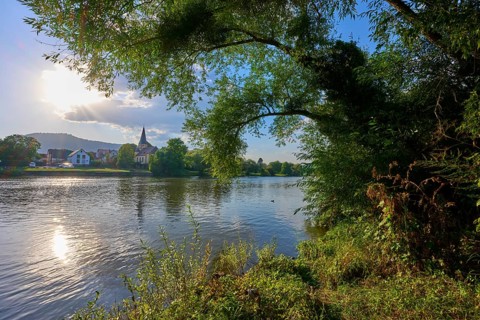 Idyllic river landscape with church in the background and lush vegetation on the banks, autumn,