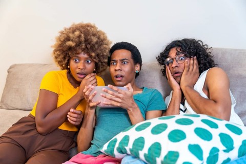 Multi-ethnic friends watching horror movie and eating pop corn sitting on the sofa at home