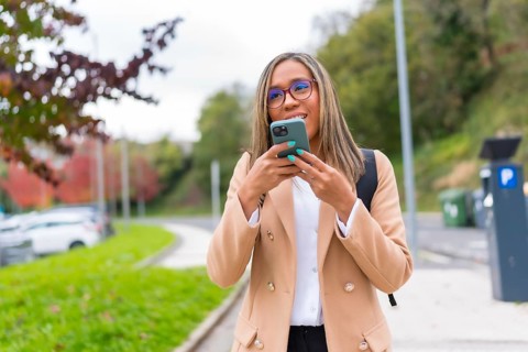 Latin woman in casual business clothes sending voice message using phone walking along the city