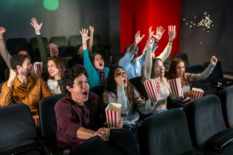 People enjoying a movie, raising hands and cheering while eating popcorn in a dark movie theater