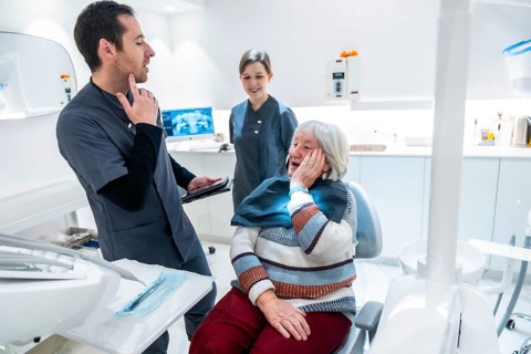 Senior woman suffering from toothache discussing treatment options with dentist and nurse in a