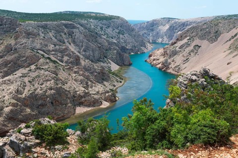 The river meanders through a stony gorge with turquoise blue water, surrounded by green trees,