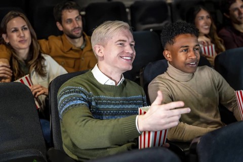 Group of diverse friends watching a film at the movie theater, commenting the scene and smiling,
