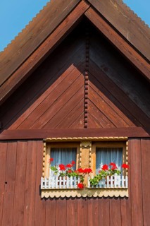 Close-up of a wooden window with red flowers under a blue sky, gable, Old wooden house, Vesec u