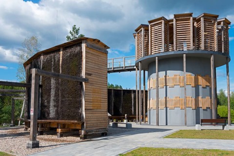 Modern wooden construction with round tower and evaporating walls, clear blue sky with clouds,