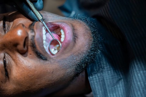 Dentist wearing black gloves using a dental mirror to examine patient's teeth during a checkup at a