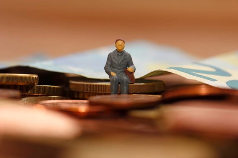 Miniature man sitting on euro coins, twenty euro note in the background, North Rhine-Westphalia,