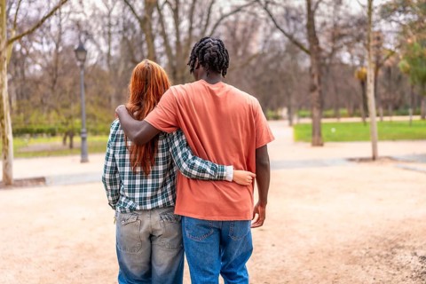 Young multi ethnic couple walking together in a park with arms around each other, enjoying a