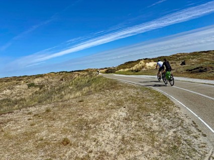 Cyclist on a wide cycle path through a dune landscape under a blue sky with clouds, north sea Cyle
