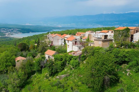 View of a village with red roofs, embedded in green vegetation and with mountains in the