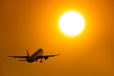 Silhouette of an aircraft taking off in front of a bright orange sunset