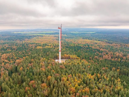 A wind power tower rises above an autumnal forest, shrouded in mist, into a wide landscape, wind