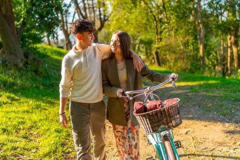 Young couple walking hand in hand through a picturesque park, riding a bicycle and basking in the