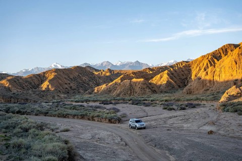Off-road vehicle driving through a canyon, landscape of eroded hills at sunrise, badlands, white