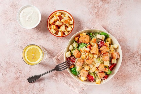 Caesar salad with salmon, with croutons and dressing, in a salad bowl, on a pink table